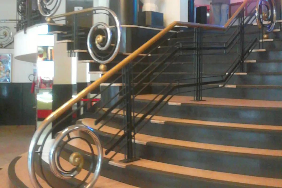 A curved staircase with dark steps and Art Deco handrails that end in polished metal spirals